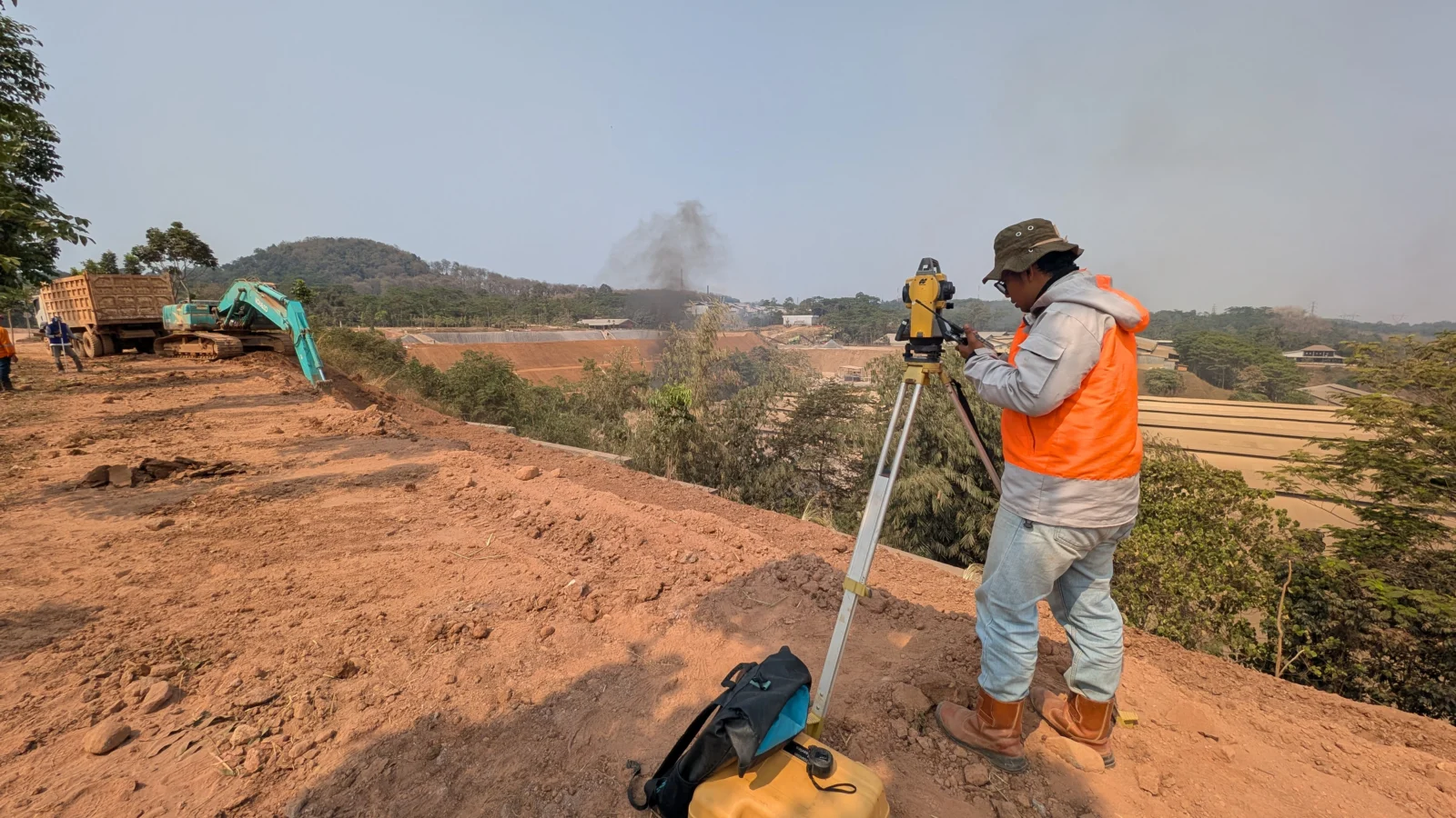 Surveyor mengukur dengan total station di dekat pekerjaan galian dengan alat berat